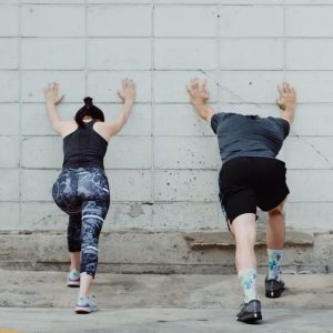 A man and woman in sportswear stretching against a wall for exercise outdoors.